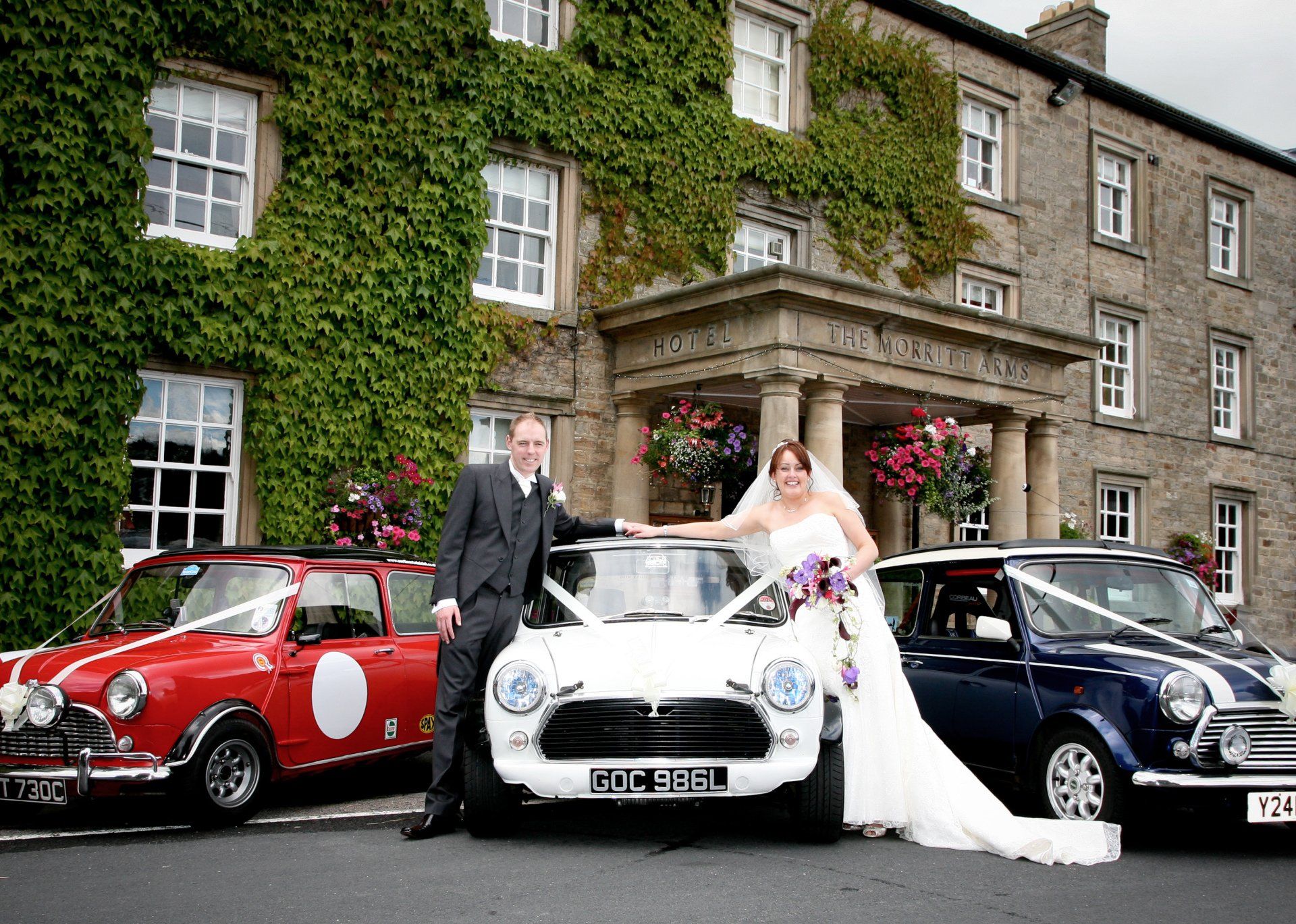 outside the morritt with 3 vintage mini cars with bride and groom smiling at the camera