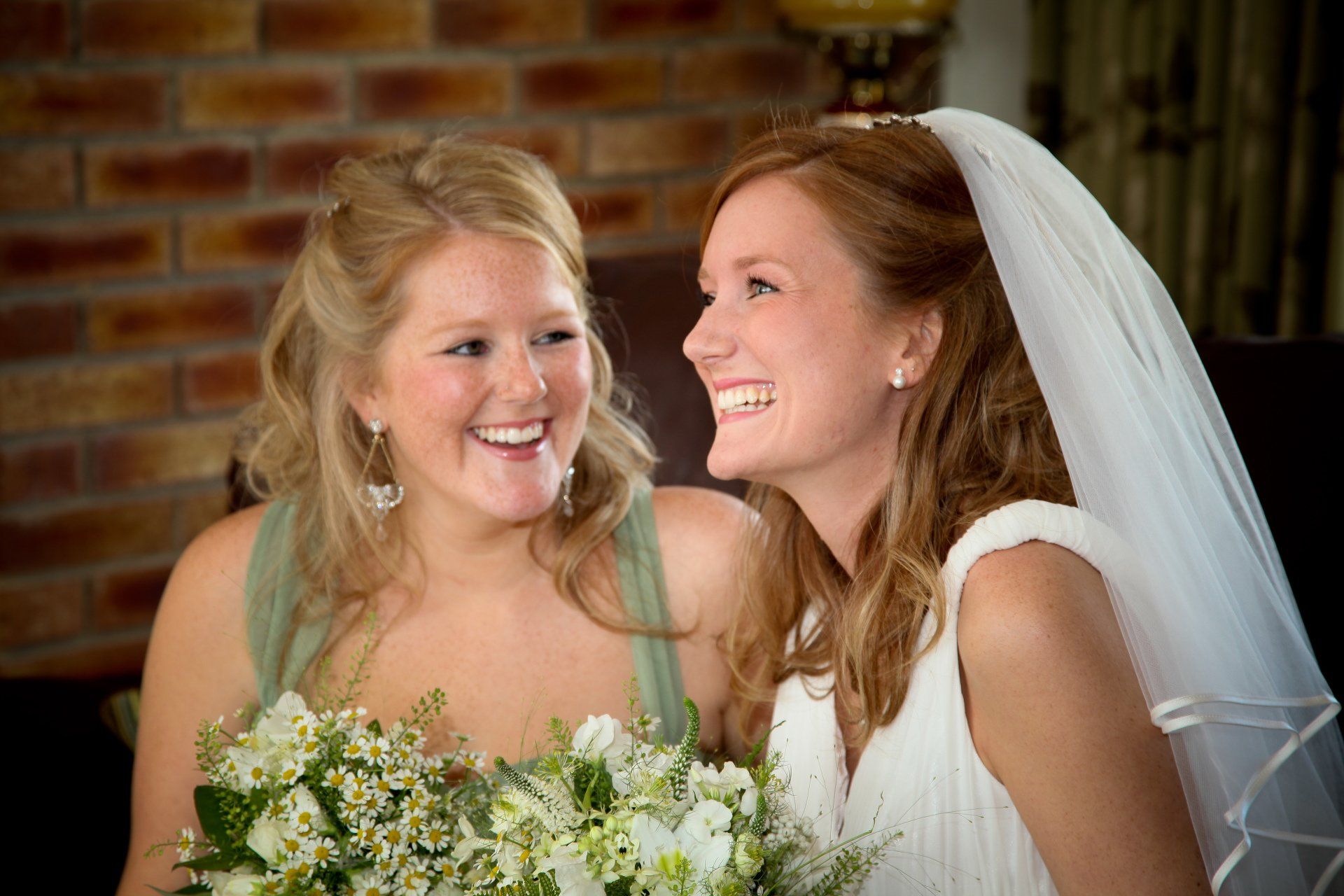 bride and sister laughing before wedding, looking away from camera