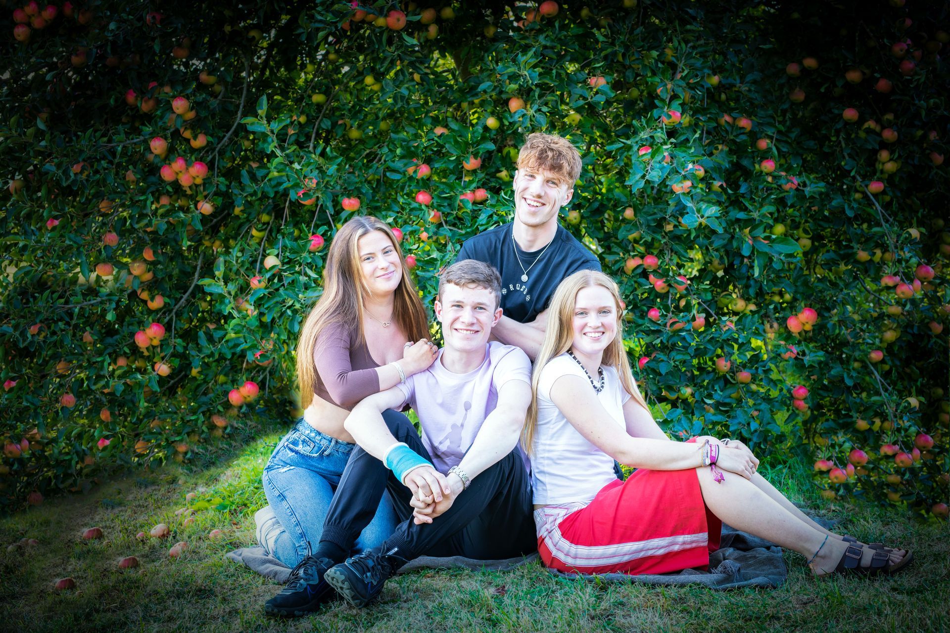 4 cousins sitting down and smiling at the camera ub county durham with apple tree behind them