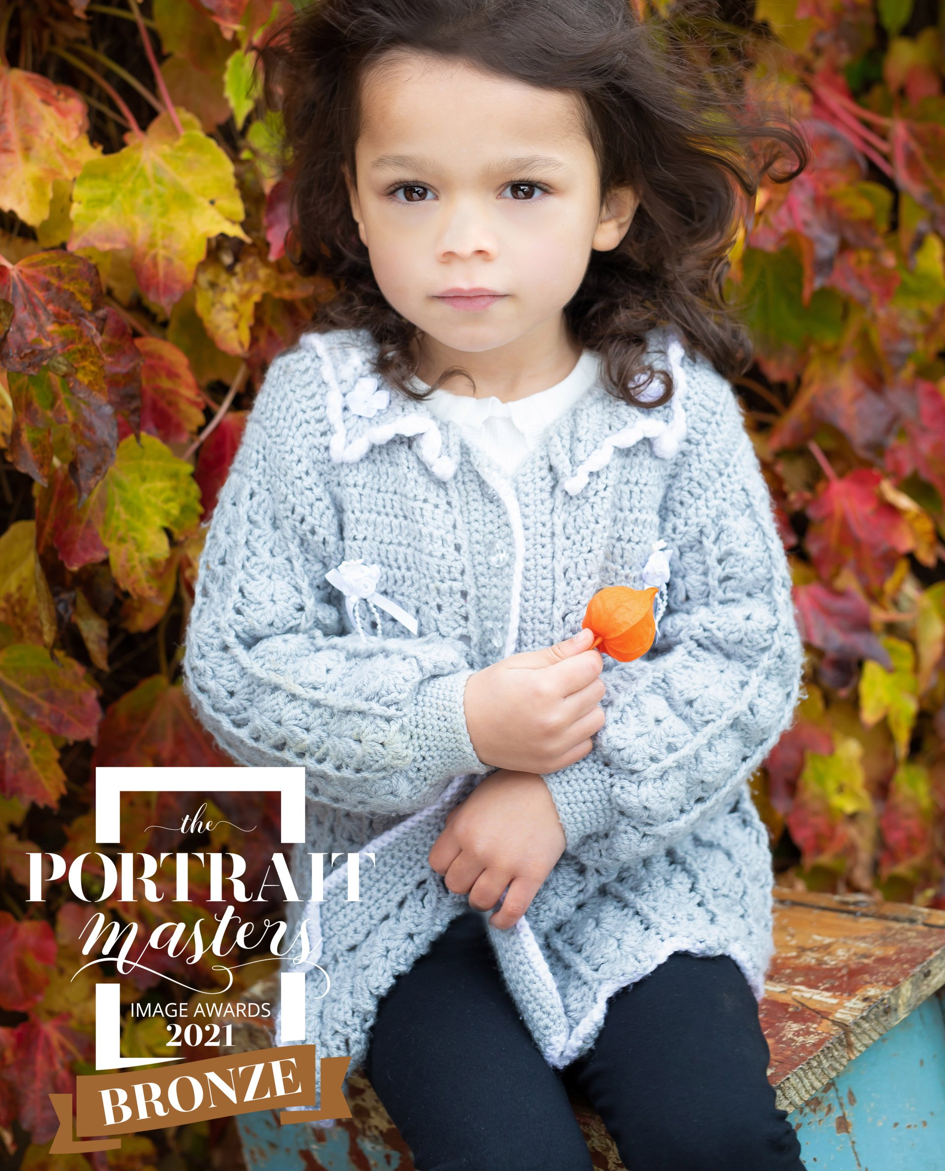 little girl looking at camera holding an orange leaf taken by award winning photographer kate mitford