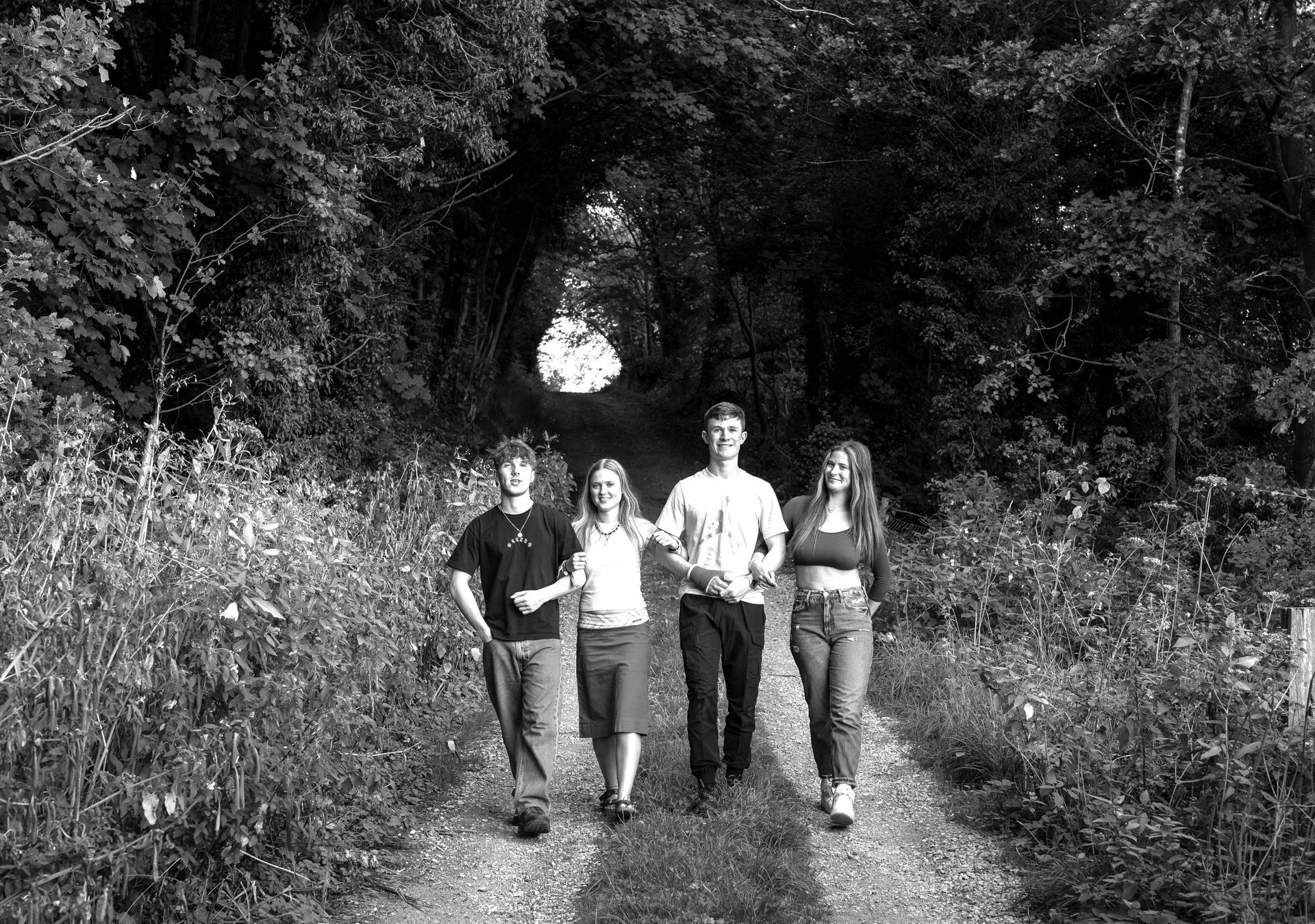 black and white image of cousins walking down a country lane all smiling at the camera and linking arms with county durham photographer kate mitford