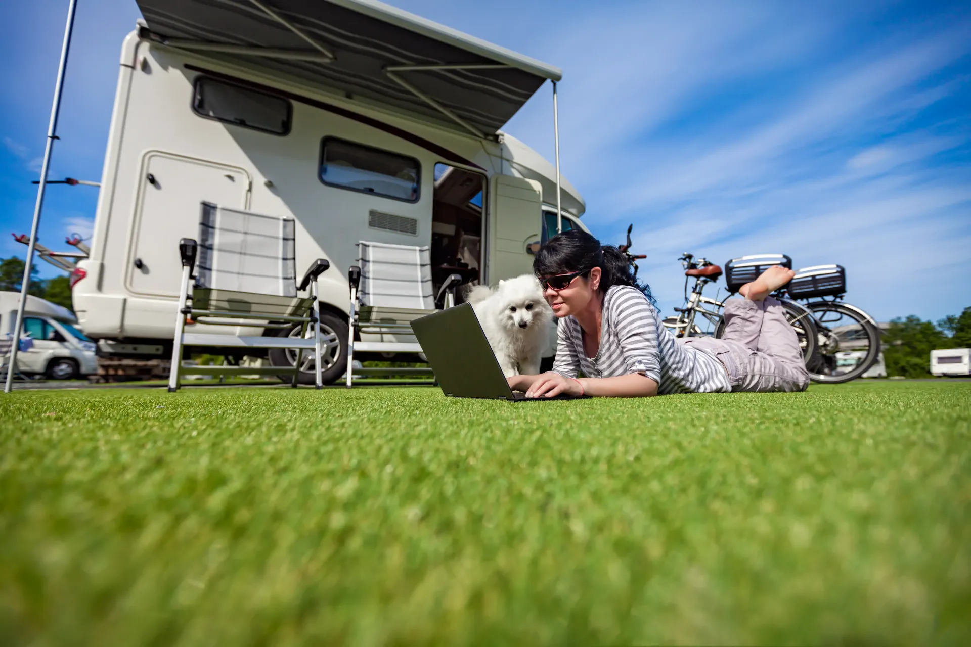 Entspannte Atmosphäre auf dem Ostseecamp Lehmberg: Eine Frau genießt das ruhige Camping-Leben mit ihrem Hund auf dem Rasen, während sie an einem Laptop arbeitet. Bei uns finden Sie Gelassenheit und Freude an der Ostseeküste in Waabs, Schleswig-Holstein.