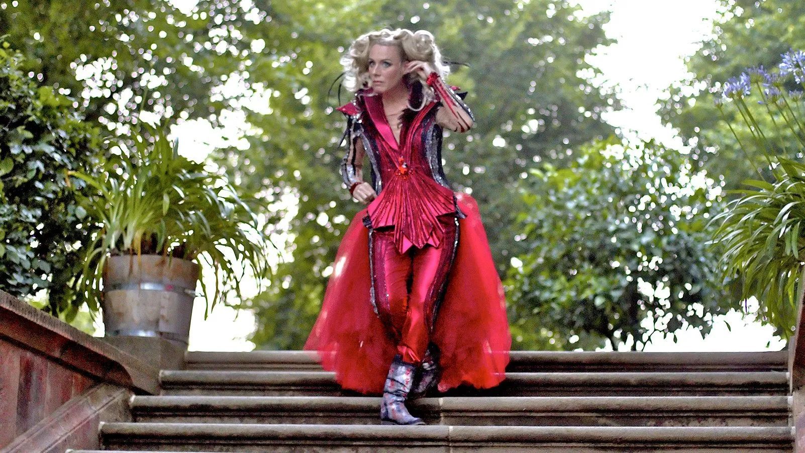 Sängerin im roten Kostüm auf einer Treppe im Park