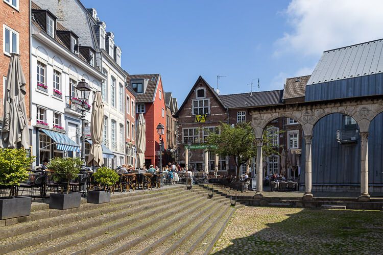 Der Hof in Aachen mit all seinem Charme. Der Hof in Aachen ist dreieckig anlegt. Hier sind viele Cafés, Stufen führen hinunter auf eine kleine Fläche, wo sich die Nachbildung eines römischen Portikus befindet.