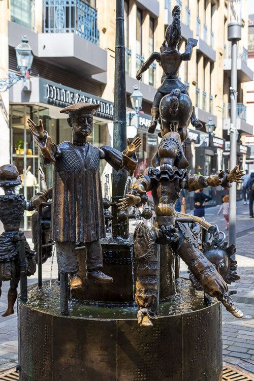 Puppenbrunnen mit Gelehrten und Harlekin. Der Puppenbrunnen zeigt verschiedene Figuren aus Bronze aus der Aachener Gesellschaft und Kultur. Hier sind Gelehrter und Harlekin zu sehen.