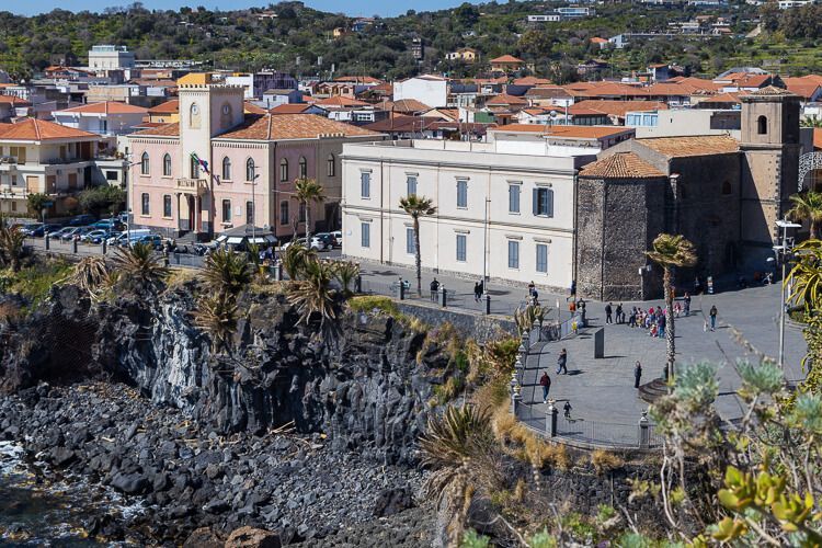 Aci Castello an der Uferzone mit schwarzem Basalt Blick auf die Promenade und schwarzes Basaltgestein am Ufer von Aci Castello.