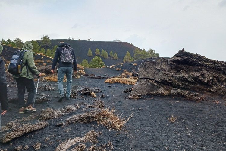 Trittfestes Schuhwerk ist für eine Ätna-Tour notwendig Eine geführte Wandergruppe läuft auf dem Ätna über Aschegranulat.