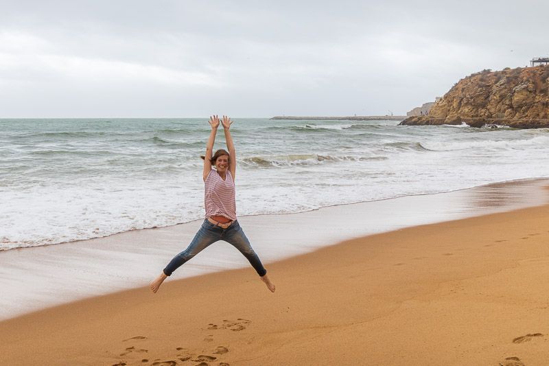 Das Wetter in Albufeira tut der Laune keinen Abbruch Eine Frau springt am Strand von Albufeira in Luft und spreizt Arme und Beine.