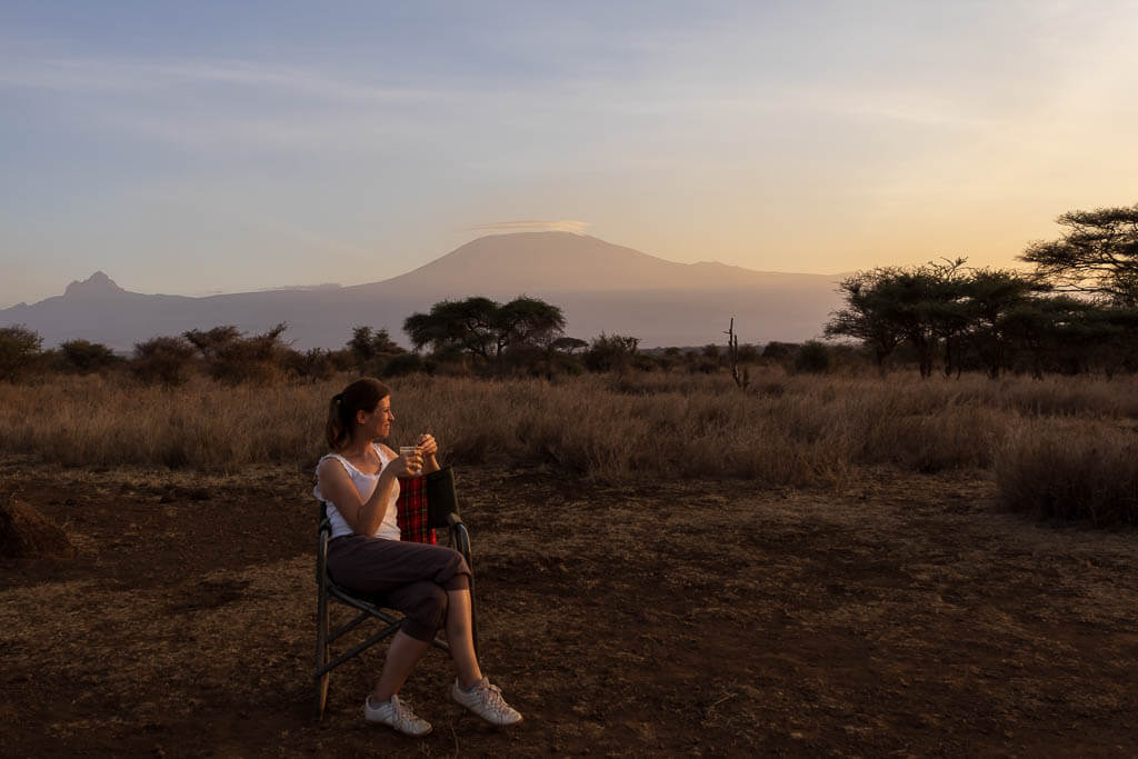 Sundowner in Amboseli Eine Frau sitzt in der Amboseli-Region bei einem Sundowner, im Hintergrund thront der Kilimandscharo.