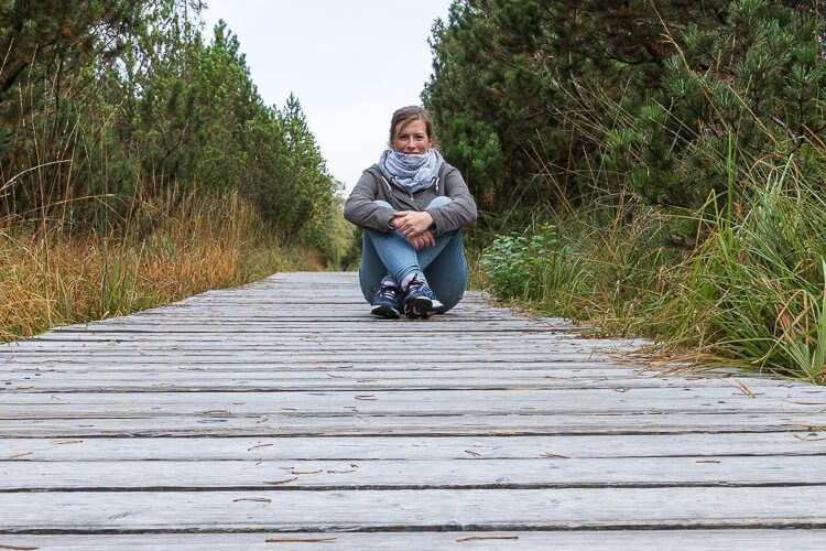 Kurzer Fotostopp, als ich mich auf dem Holzweg im Wildseemoor befinde. Eine Frau sitzt auf dem Holzbohlenweg im Wildseemoor um ein Foto zu schießen. Rechts und links ist üppige Vegetation.