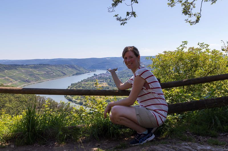 Ein Plätzchen im Schatten mit toller Sicht auf Weinberge und die große Rheinschleife. Eine Frau an einem Aussichtspunkt auf die große Rheinschleife, dem Bopparder Hamm. Das Wetter ist schön und klar.