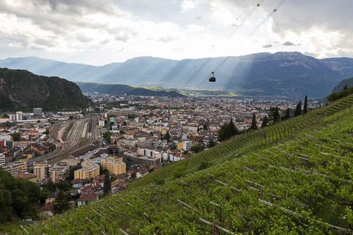 Blick auf Bozen mit Seilbahn von der Oswaldpromenade aus, die Sonne bricht durch die Wolken.