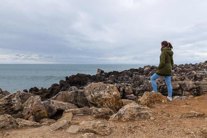 Auf meinem Weg zum Boca do Inferno Eine Frau steht an einer felsigen Küste bei Cascais und blickt aufs Meer.