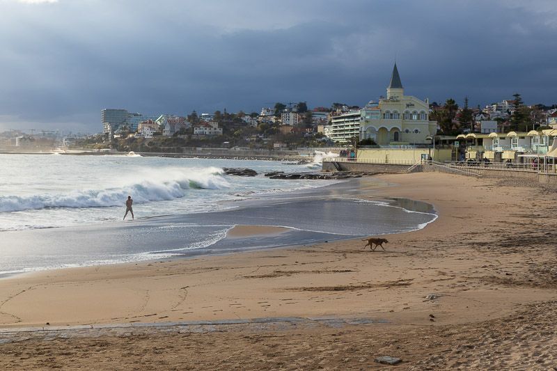 Beeindruckende Strandkulisse bei Cascais Strand bei Cascais. Eine Person steht bei starkem Wellengang am Strand. Dunkle Wolken ziehen auf.