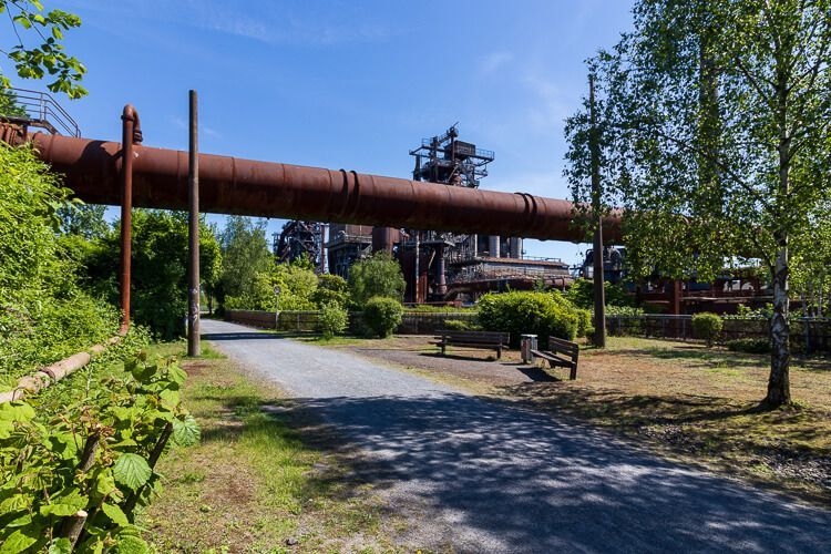 Rundgang durch den Landschaftspark Duisburg-Nord Ein dickes rostiges Rohr verläuft oberhalb eines Spazierweges im Landschaftspark Duisburg-Nord.