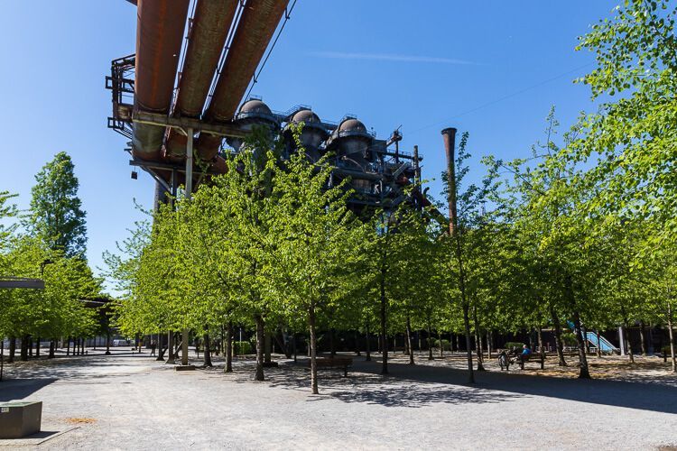 Natur und Industrie bilden eine tolle Kulisse Gelände des Landschaftspark Duisburg-Nord mit dicken rostigen Rohren und jungen grünen Bäumen als Kontrast.