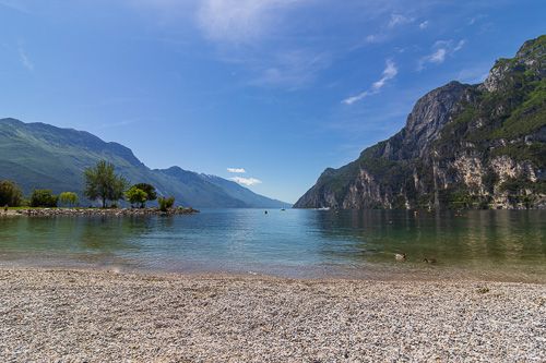 Am Strand von Riva del Garda im Norden des Gardasees. Rechts und links sind Berge, während der See in den schönsten Farben schilltert.