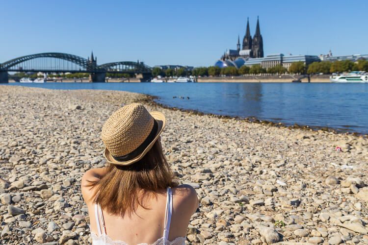 Ein sonniger Tag am Rhein. Frau sitzt bei Sonnenschein am Rheinufer und blickt auf den Kölner Dom und die Hohenzollernbrücke.