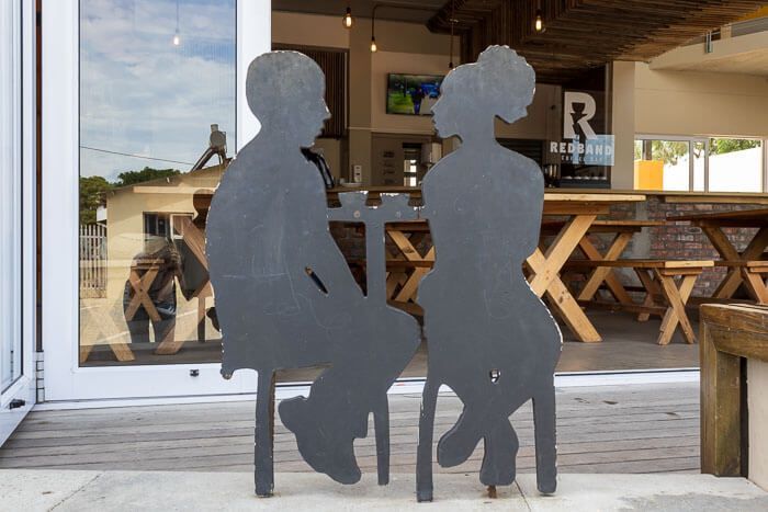 Freundlich gestalteter Eingangsbereich von MyMito. Vor dem MyMito in Walmer Township. Zwei Aufsteller, die an einem Bistrotisch sitzen, symbolisieren für mich die Gemeinschaft der Menschen.