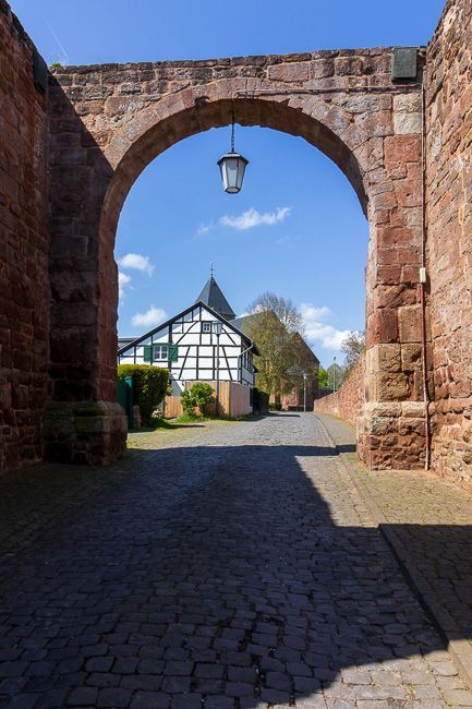 Durch ein Burgtor blickt man auf ein Fachwerkhaus und die Kirche von Nideggen.