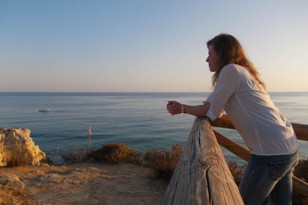 Sonnenuntergang in Portimão, Portugal, genießen. Eine Frau steht im Abendlicht am Holzgeländer an einer Klippe und genießt den Sonnenuntergang.