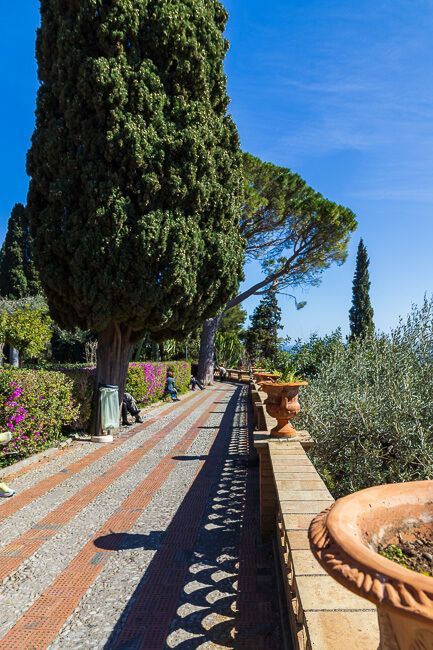 Idyllischer Weg mit Balustrade und großen Bäumen im Giardino Pubblico in Taormina.