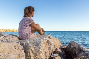 Frau sitzt auf einem Felsen und blickt auf das Meer.
