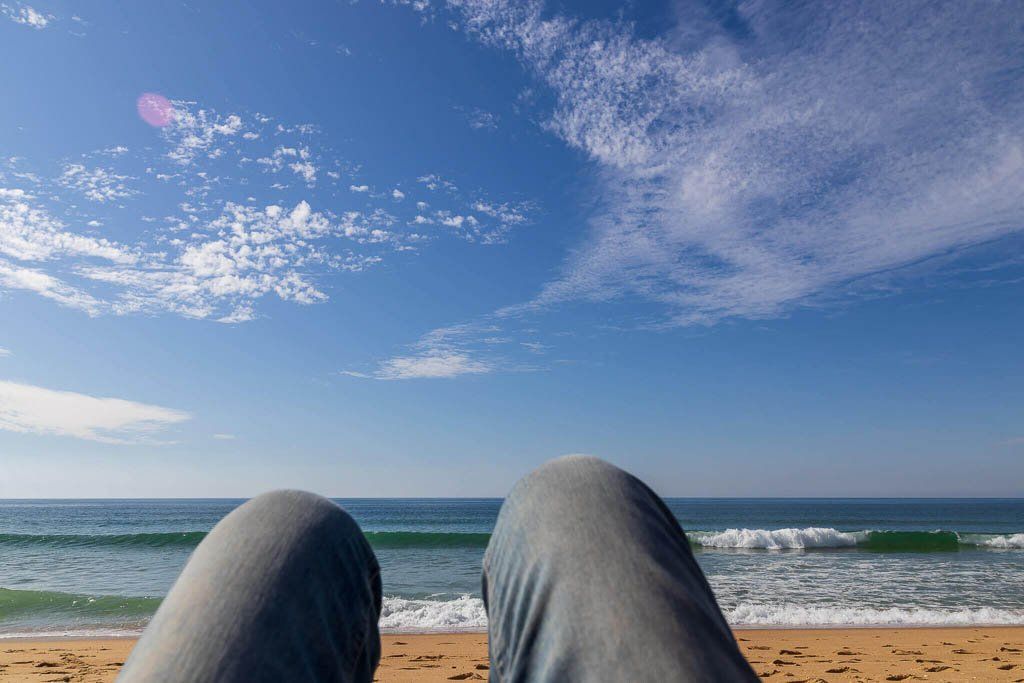 Alleine reisen als Frau in Faro, Portugal Eine alleinreisende Frau liegt am Strand von Faro und blickt in den blauen Himmel.