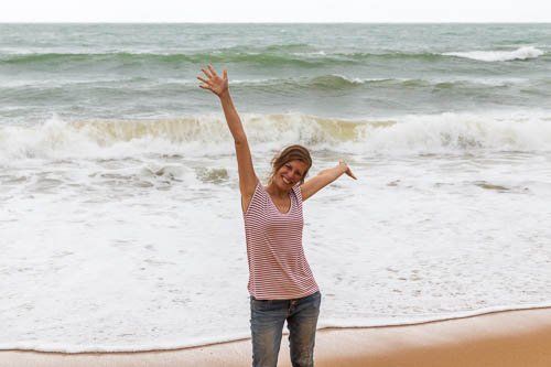 Katrin reckt glücklich die Arme am Strand von Albufeira, im Hintergrund imposante Wellen