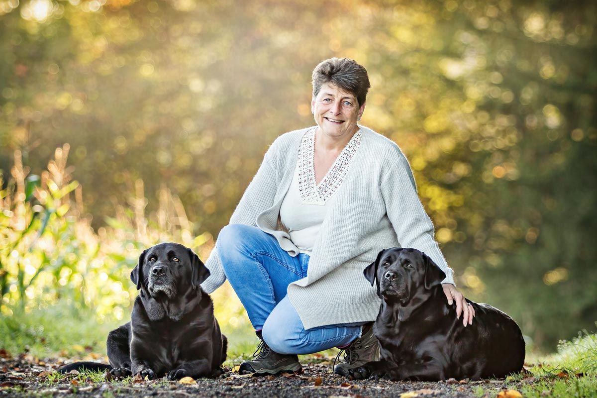 LL Photography Mensch und Tier: eine Frau mit zwei schwarzen Labradoren sitzt in herbstlicher Landschaft