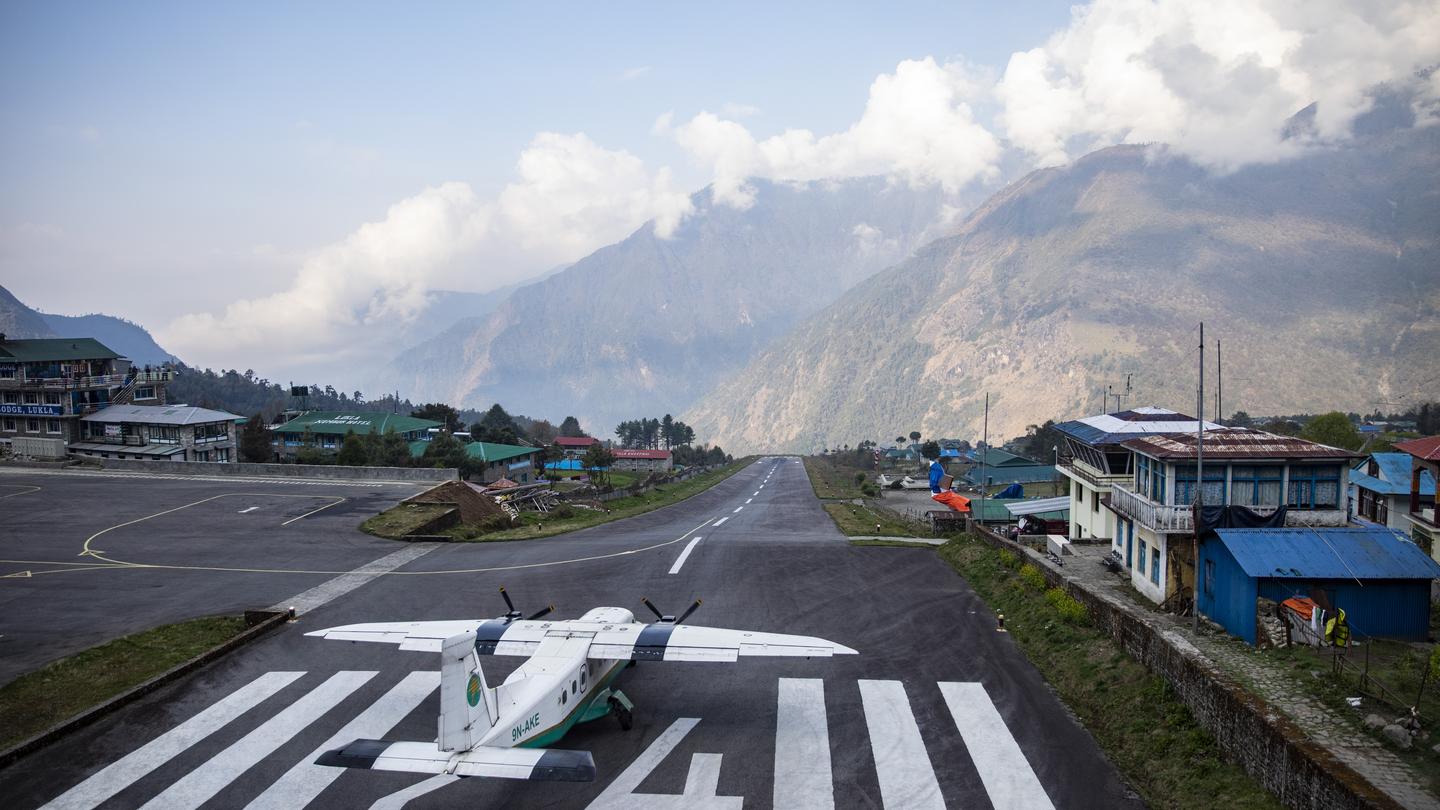 A small aircraft on the runway at Lukla Airport (Tenzing-Hillary Airport) surrounded by misty mountains.