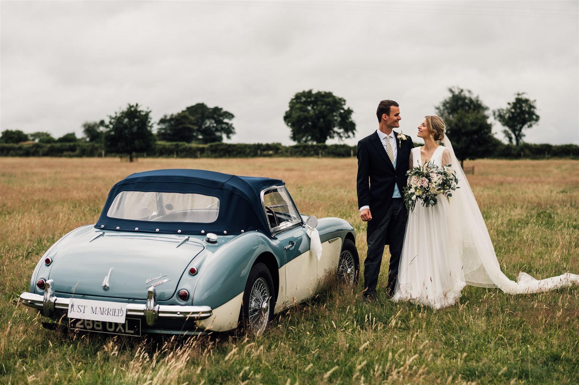 Bride and Groom stood by car at their DIY garden wedding that Tasha Mae is co-ordinating.