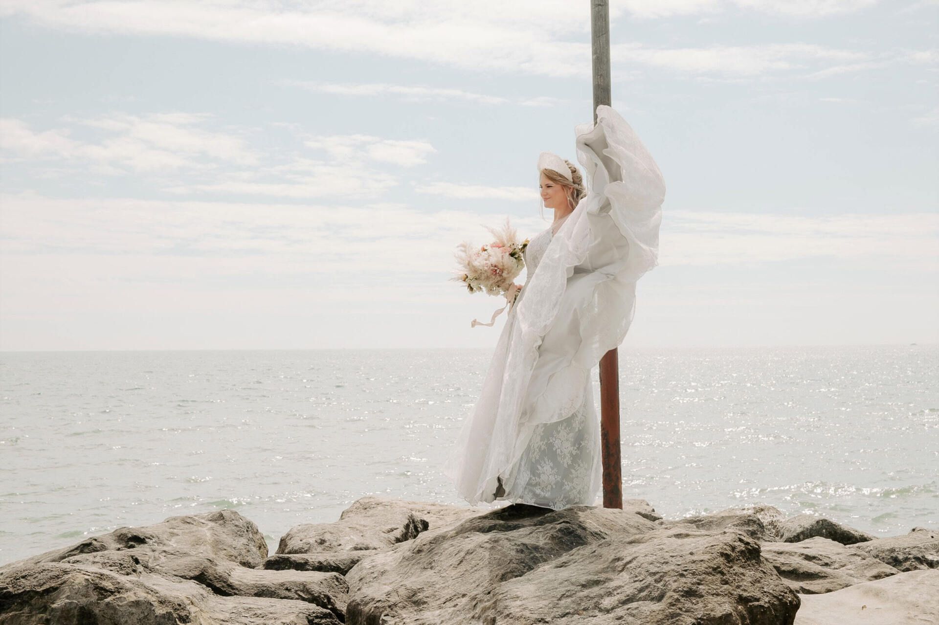 Bride stood at end of groyne holding dress up on Highcliffe Beach in Dorset