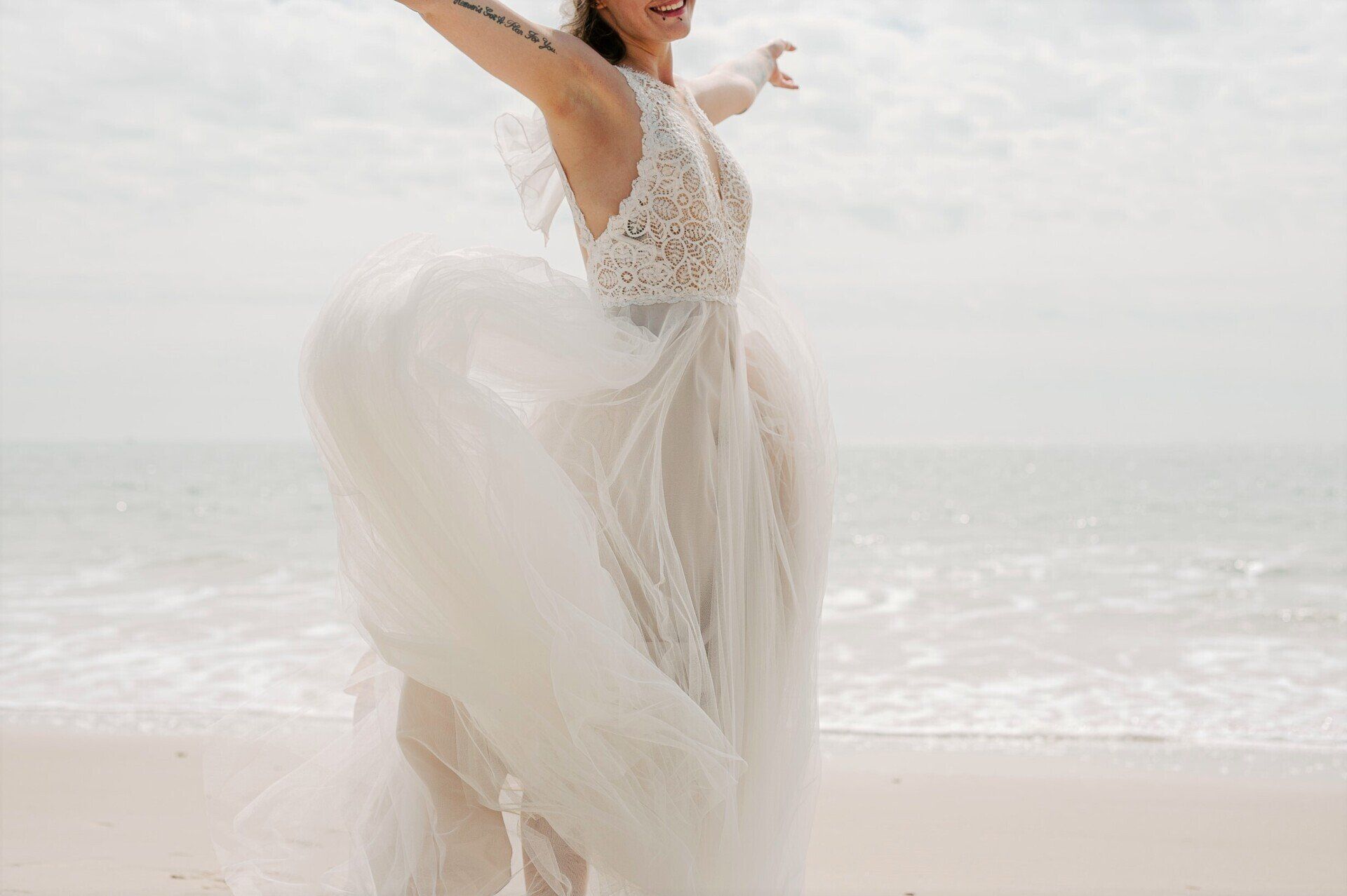 Close up of bride dancing in her wedding dress by the sea on Highcliffe Beach in Dorset