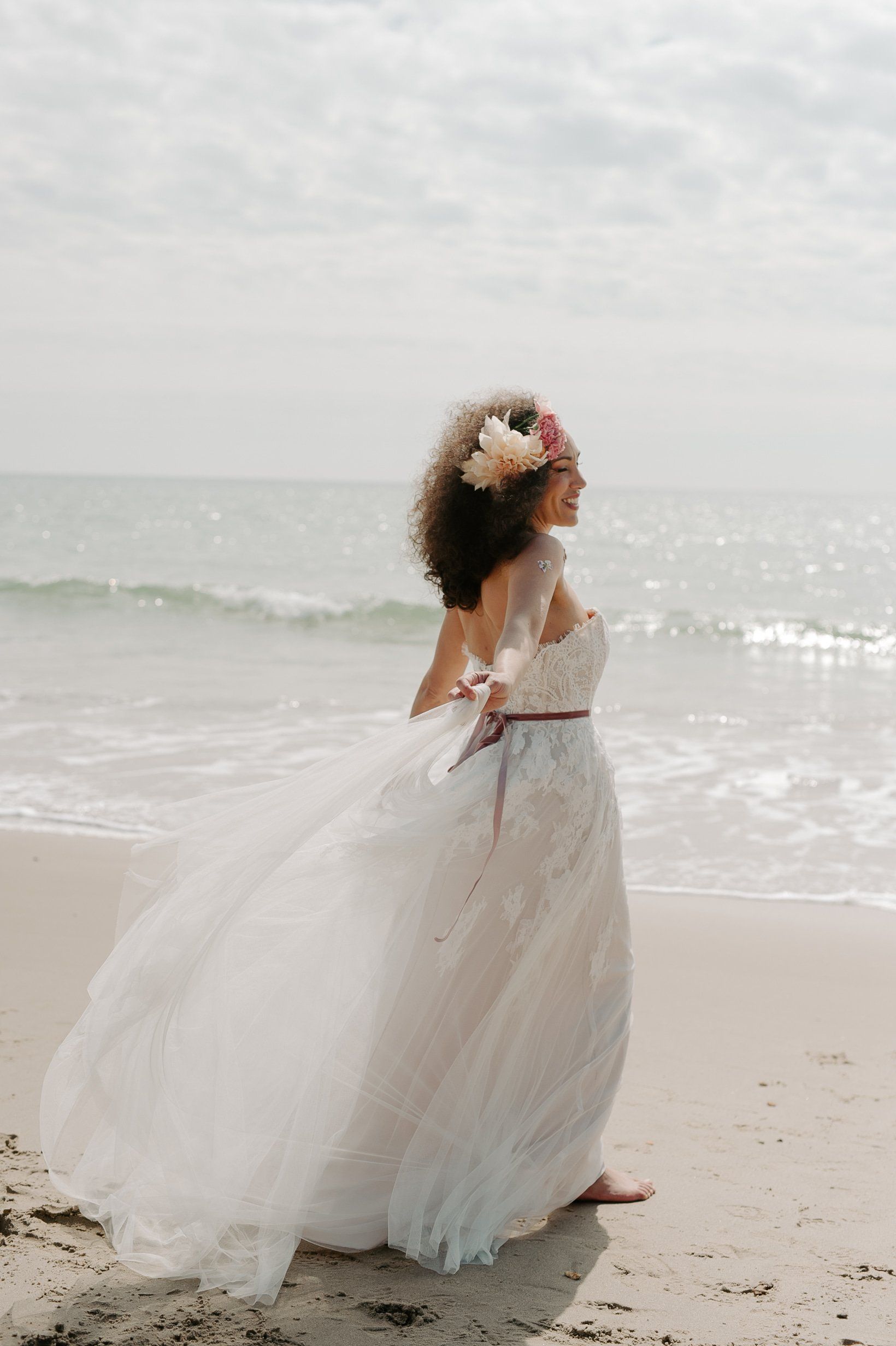 Bride walking along shoreline with se shimmering in the background on Highcliffe Beach in Dorset