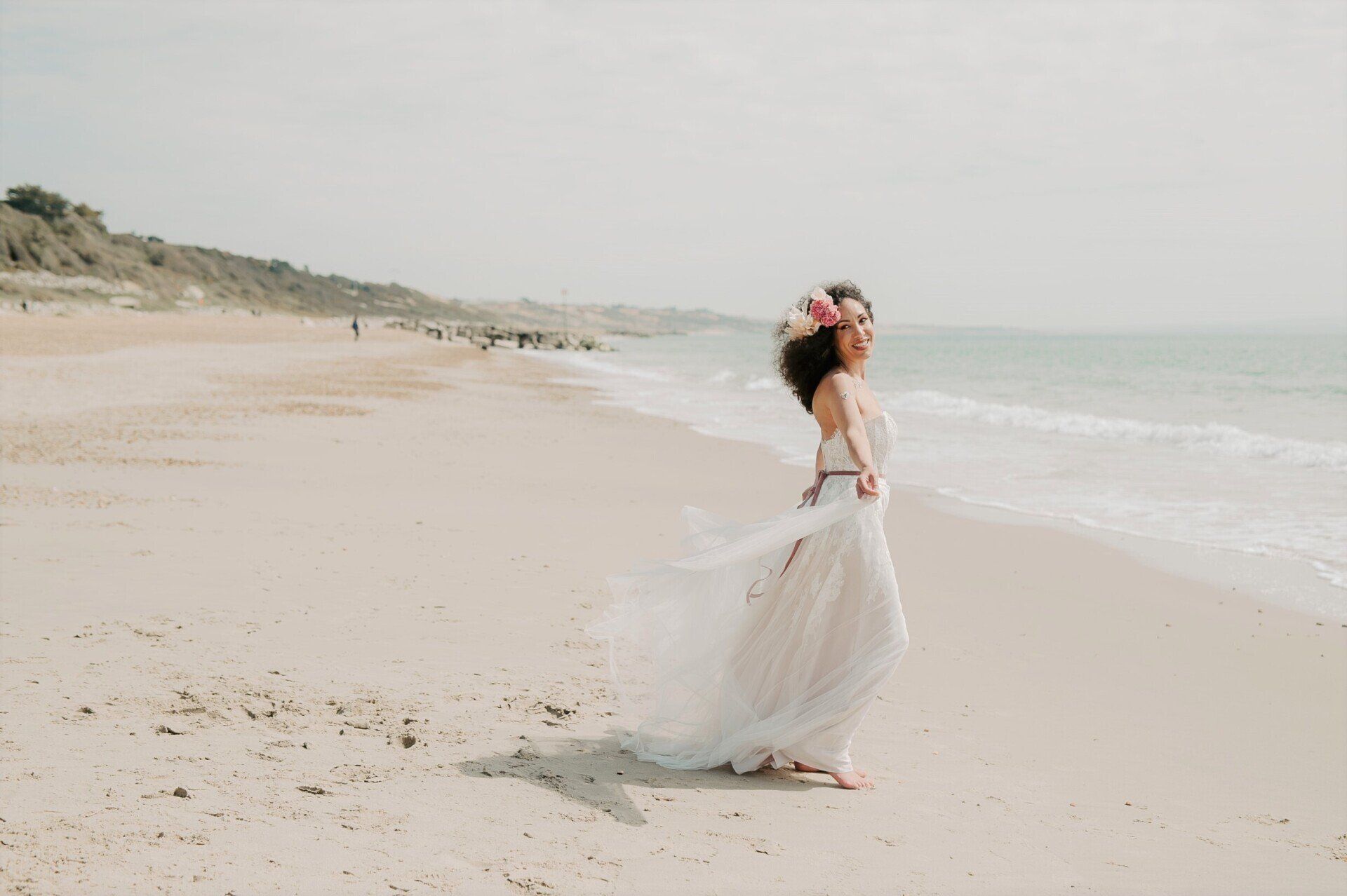 Bride walking across the sand towards the sea in her wedding dress on Highcliffe Beach in Dorset