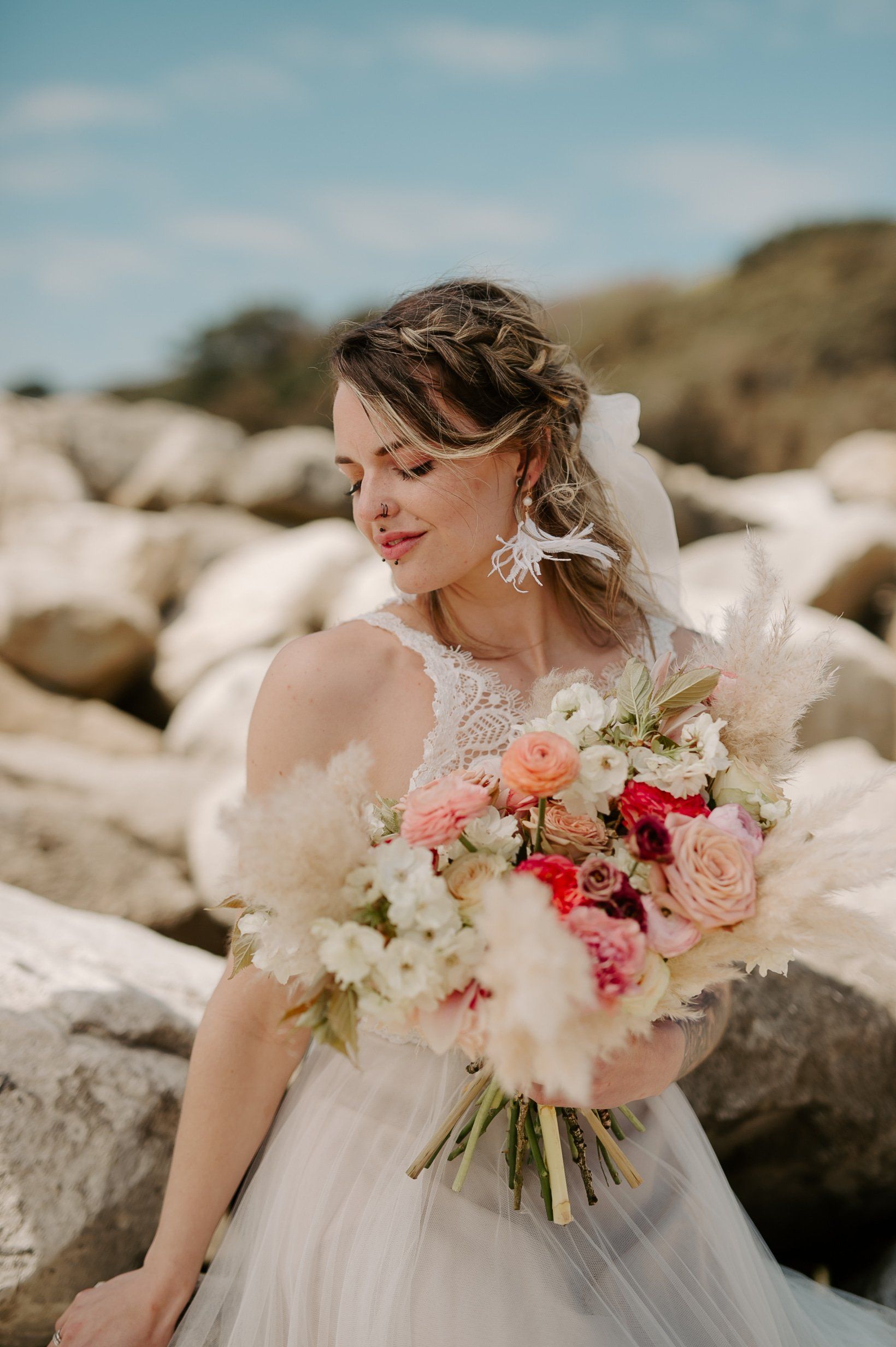 Bride in wedding dress holding bouquet wearing tassel earrings blowing in the sea breeze on Highcliffe Beach in Dorset