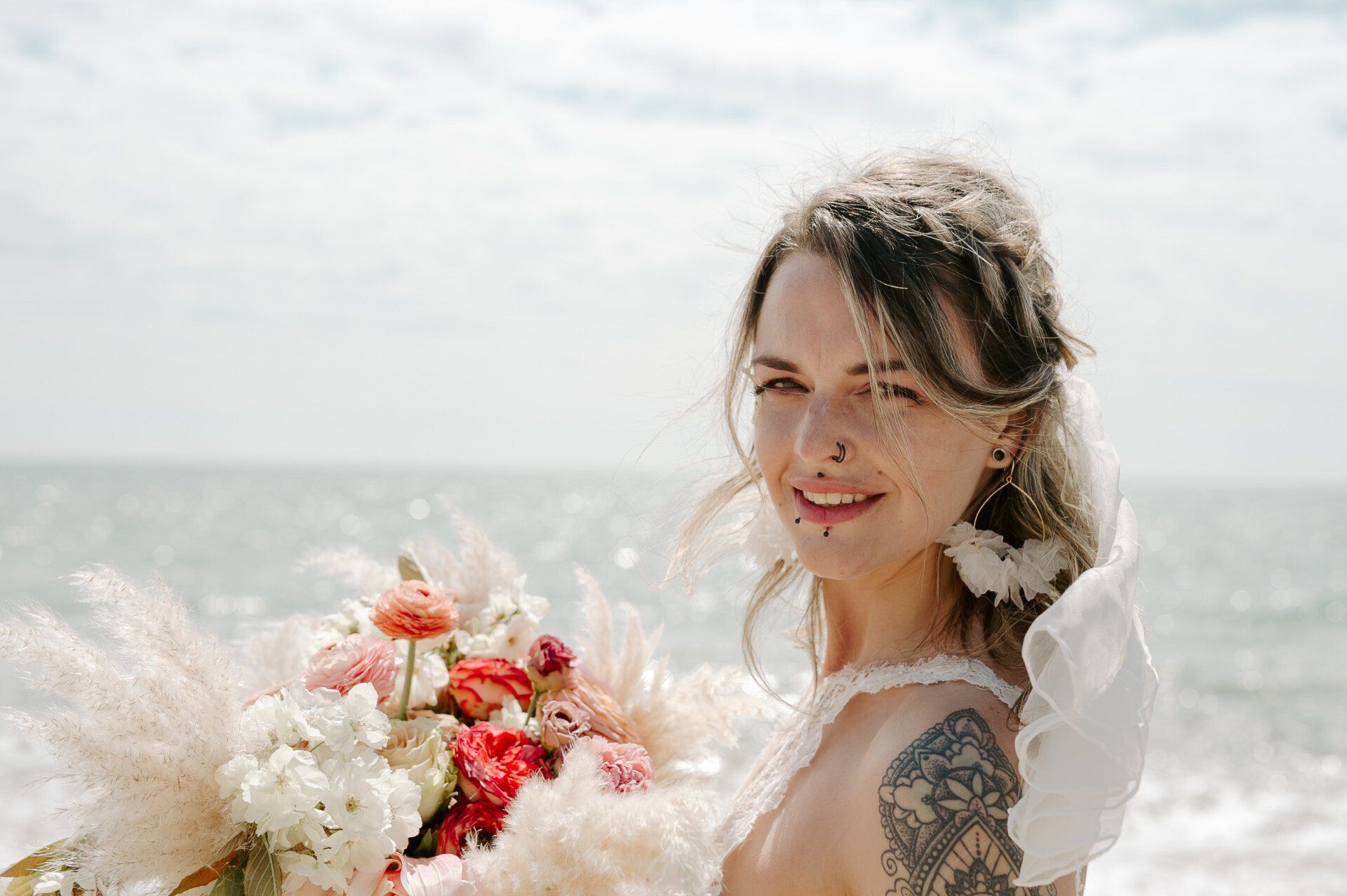Head shot of bride holding bouquet wearing large gold hoop clustered earrings on Highcliffe Beach in Dorset