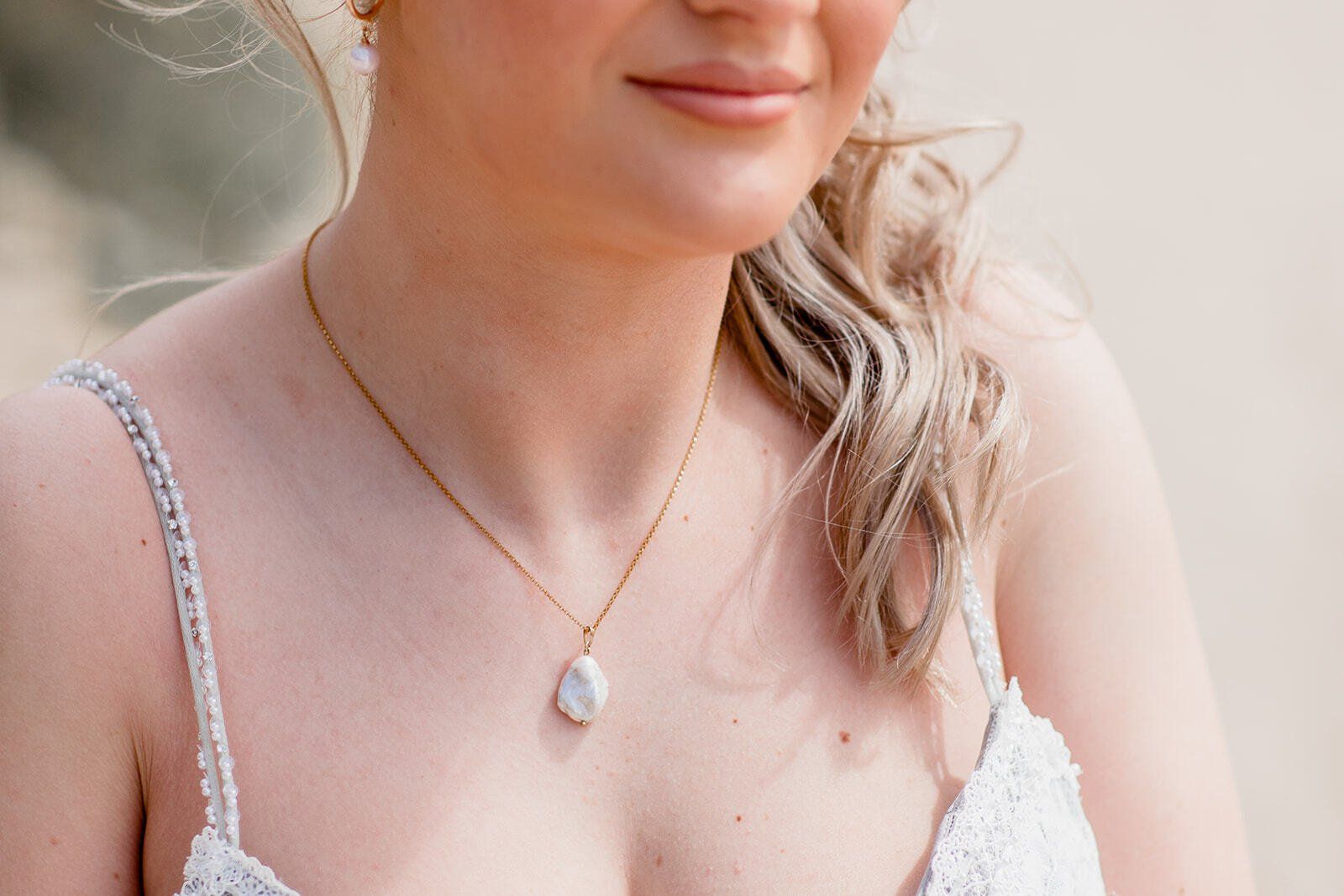 Close up of brides chest showing a gold and pearl necklace wearing a wedding dress