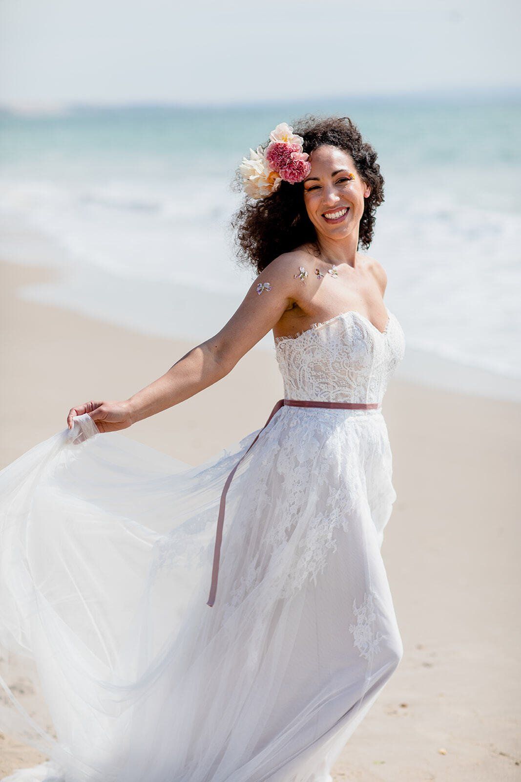 Bride walking along the shoreline holding the back of her dress up on Highcliffe Beach in Dorset