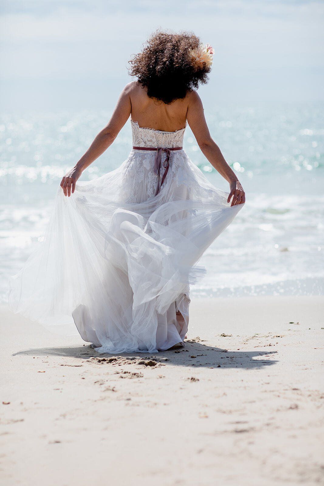 Bride wearing a wedding dress walking towards the sea at Highcliffe Beach in Dorset