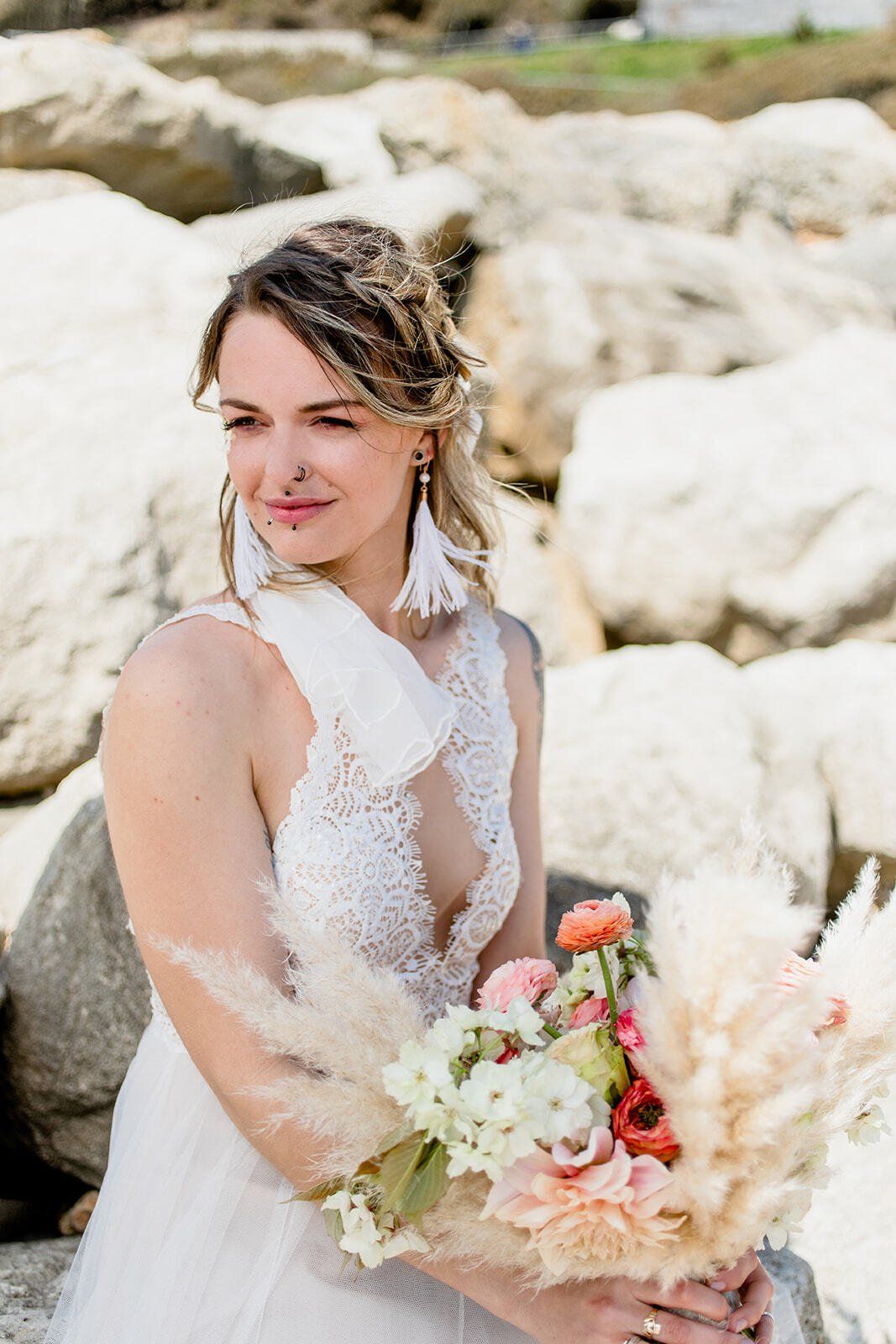 Bride wearing wedding dress holding bouquet wearing feather earrings on Highcliffe Beach in Dorset