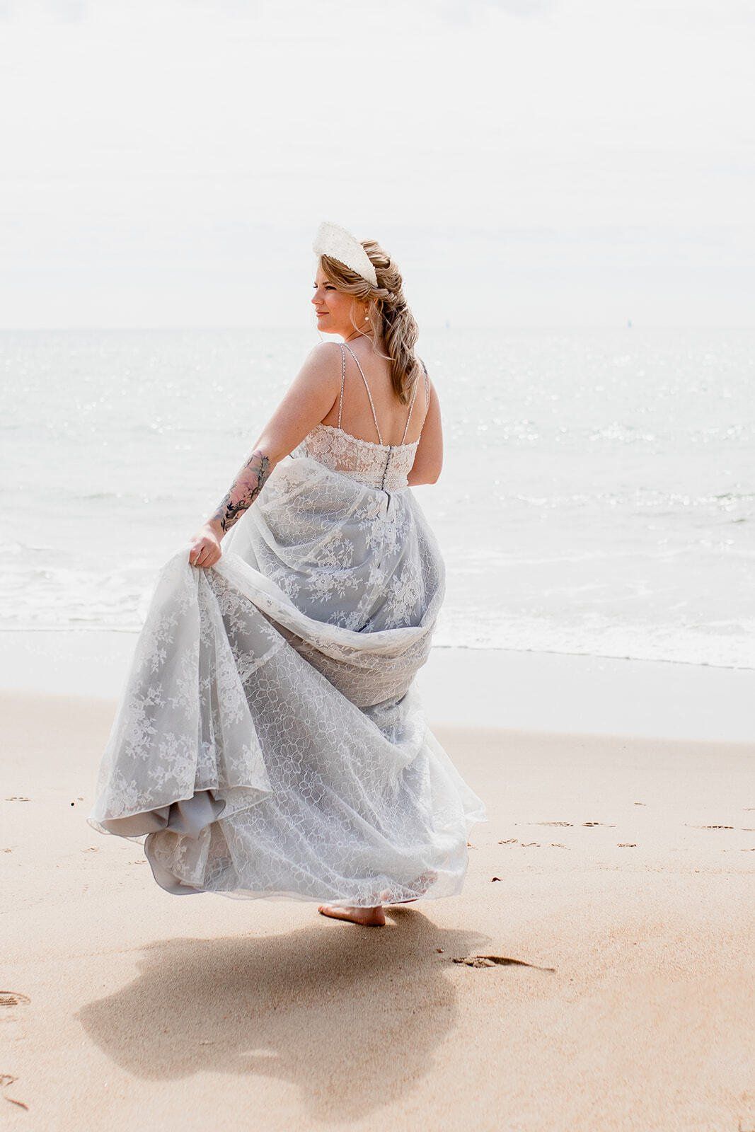 Bride walking along sand holding dress up along shoreline on Highcliffe Beach in Dorset