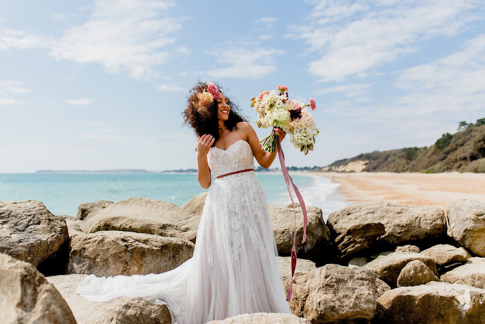 Bride stood in her wedding dress on the groyne rocks at Highcliffe Beach in Dorset holding a bouquet
