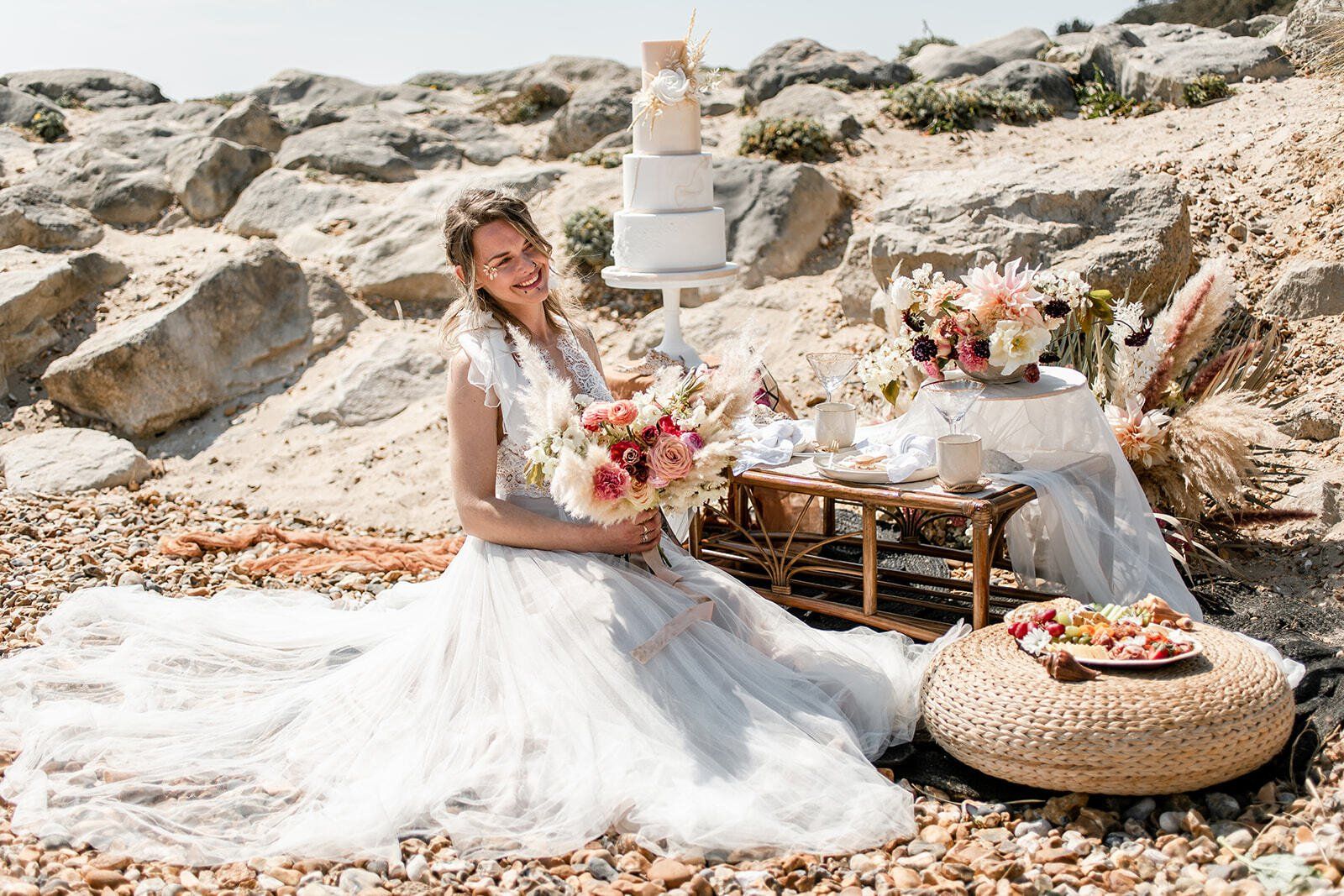 Bride sat at a bridal picnic holding a bouquet on Highcliffe Beach in Dorset