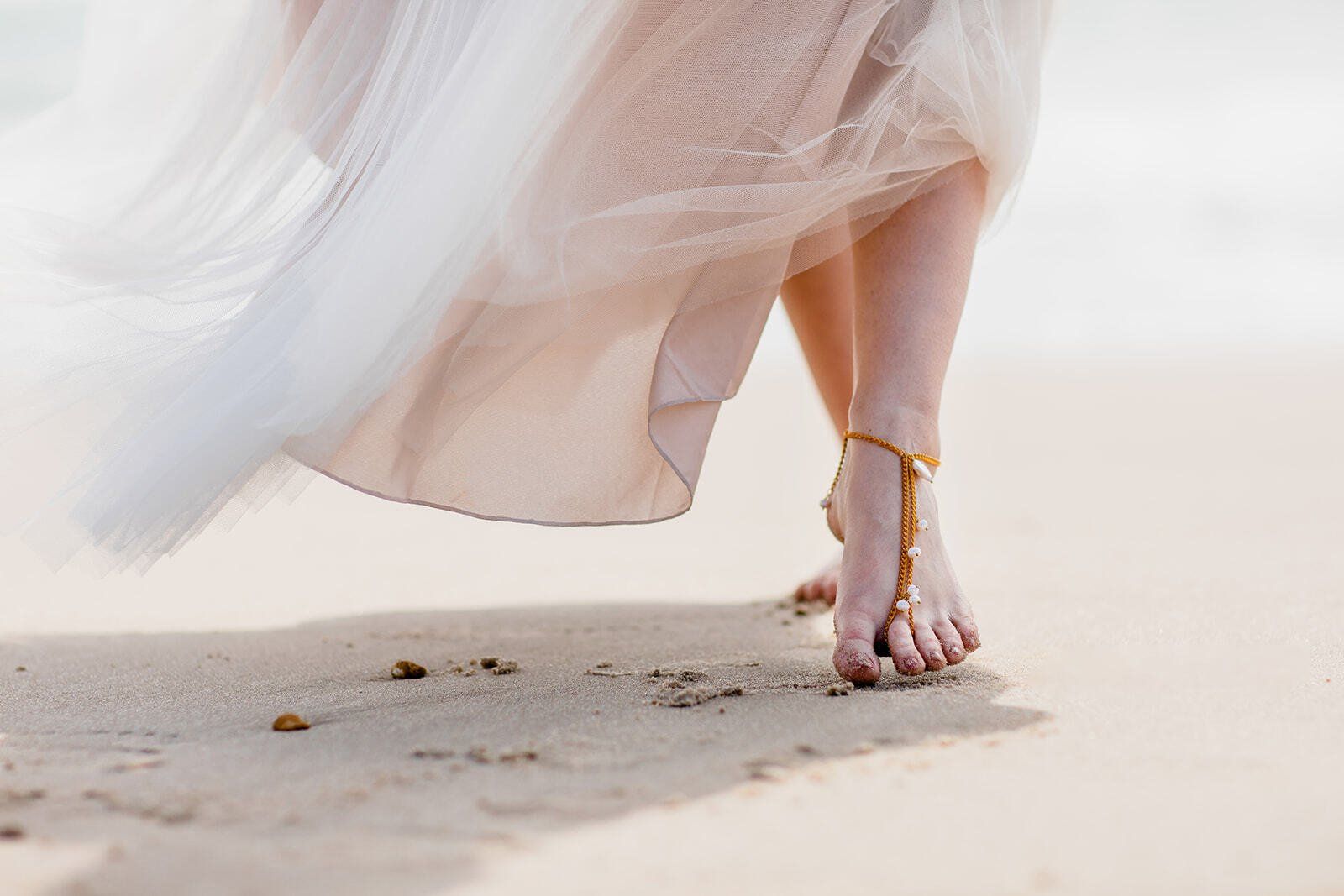Close up of brides feet wearing pearl barefoot sandals walking across the sand on Highcliffe Beach