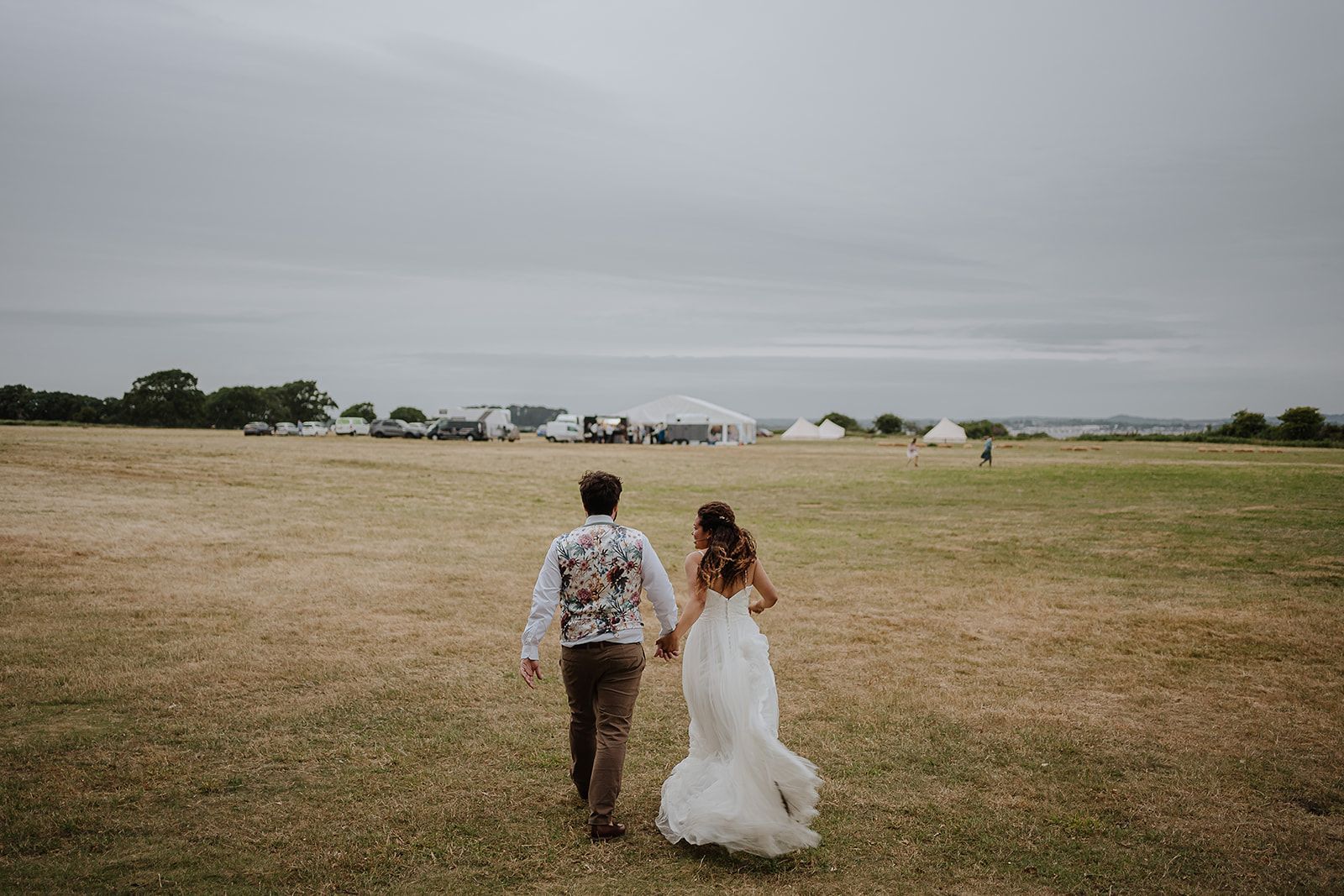 Bride and groom walking towards their wedding marquee in a field co-ordinated by Tasha Mae Wedding co-ordinator.