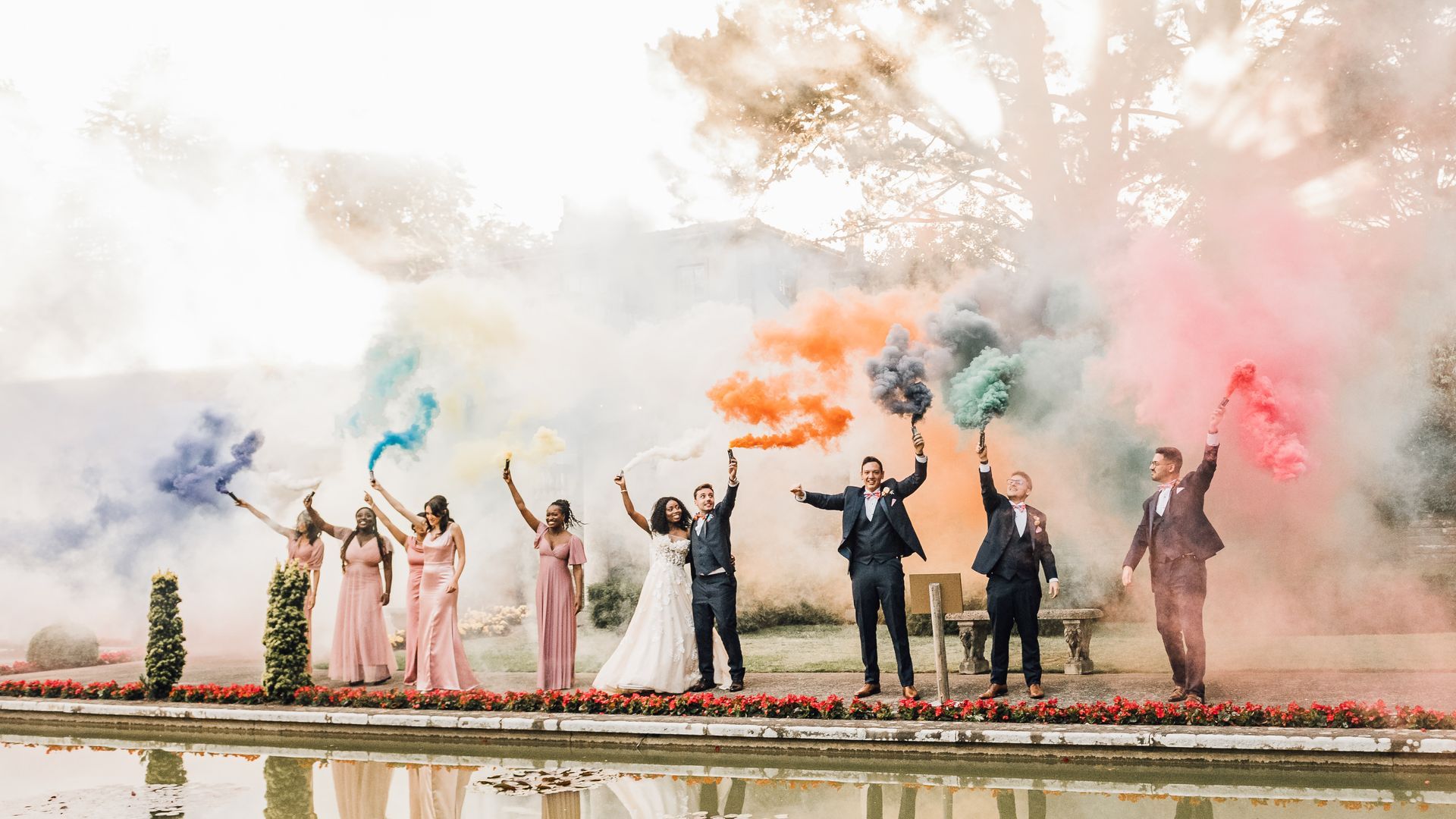 Bride and groom with their bridesmaids and groomsmen holding coloured smoke grenades at their wedding at The Italian Villa in Dorset co-ordinated by Tasha Mae Wedding Co-ordinator