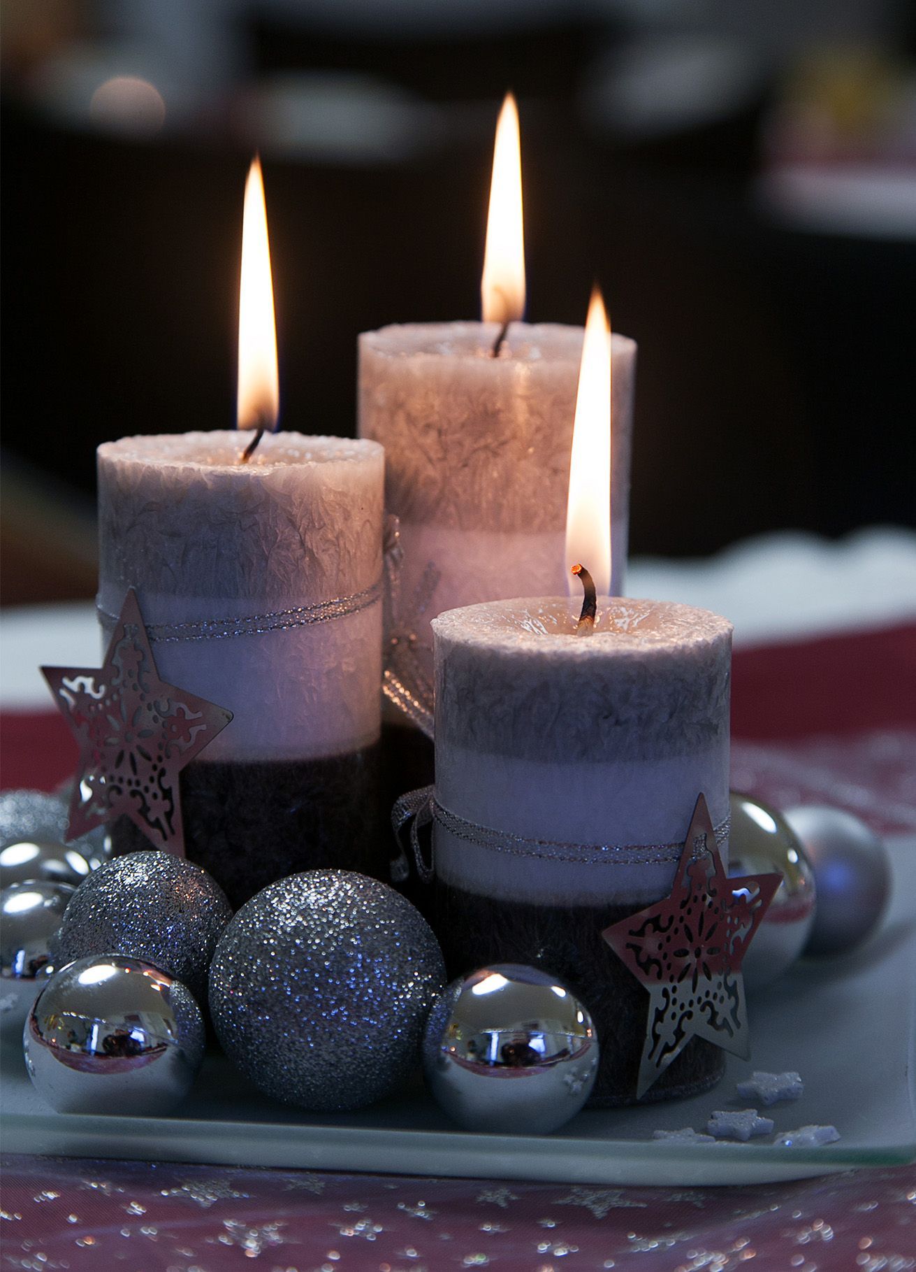 drei silberne kerzen mit weihnachtlicher dekoration brennen vor einem dunklen hintergrund
