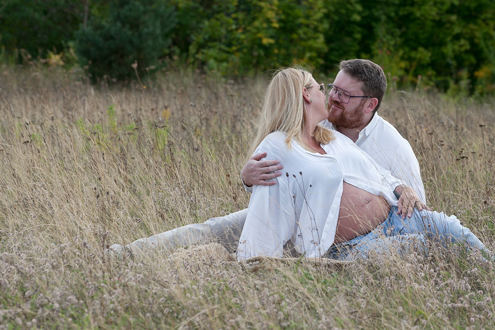 Verliebtes Paar beim Babybauchshooting am Zwenkauer See, kurz vor dem Kuss im Gras.